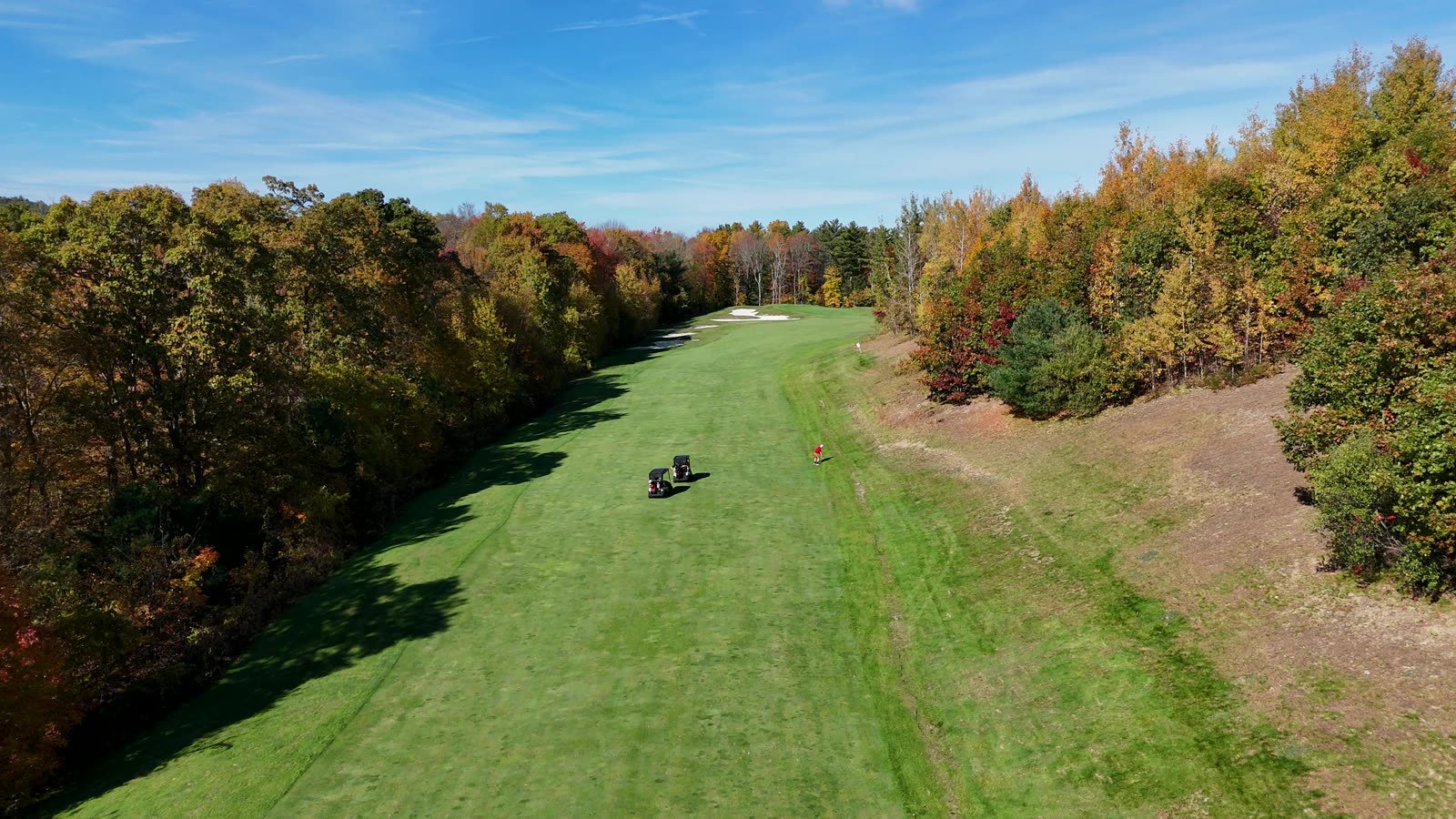 Golf fairway in fall foliage from above, two carts on the grass